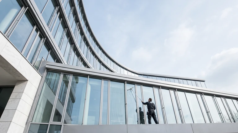Symbolbild: Fensterreiniger mit Teleskopstange an einer geschwungenen Glasfassade
